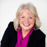 light haired woman smiling, wearing a black blazer and purple blouse